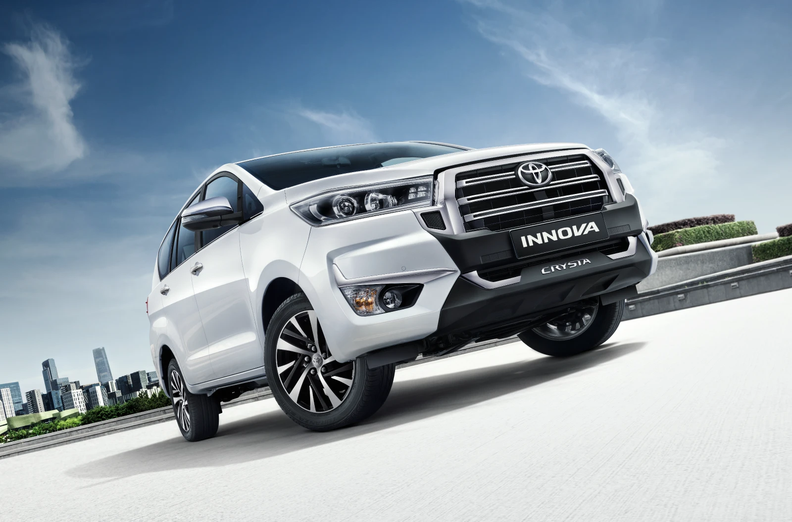 White Toyota Innova Crysta front three quarter view with city skyline